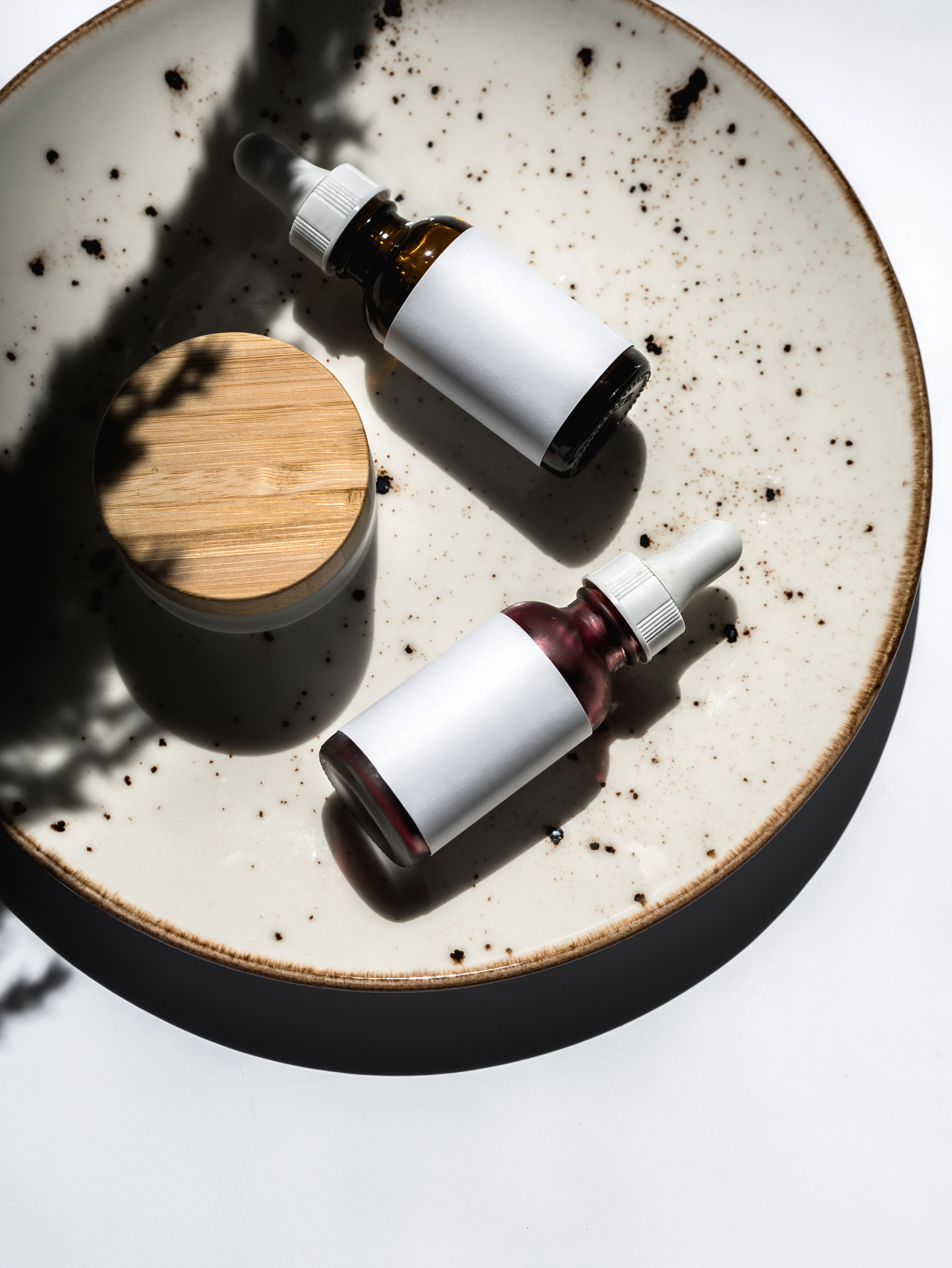 Composição flat lay de frascos de conta-gotas cosméticos em um prato de cerâmica sob luz natural.