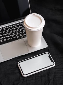 Stylish workspace featuring a laptop, smartphone, and coffee cup, creating a minimal tech vibe.