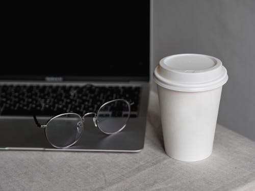 Black Framed Eyeglasses Beside White Disposable Cup