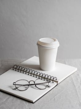 A simple workspace featuring a disposable coffee cup, notebook, and eyeglasses.