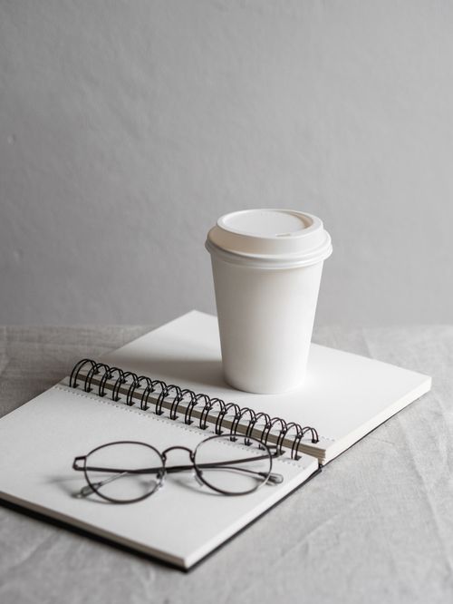 Free A simple workspace featuring a disposable coffee cup, notebook, and eyeglasses. Stock Photo