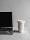 Disposable Cup Near Eyeglasses and Laptop