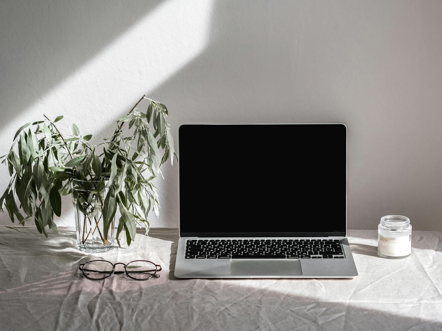 A clean and bright minimalist workspace featuring a laptop, eyeglasses, and a plant