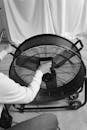 Grayscale Photo of Person Turning on an Industrial Fan