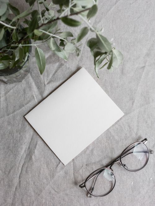 Free A clean, minimalist flatlay with eyeglasses, a plant, and a paper on a linen surface. Stock Photo