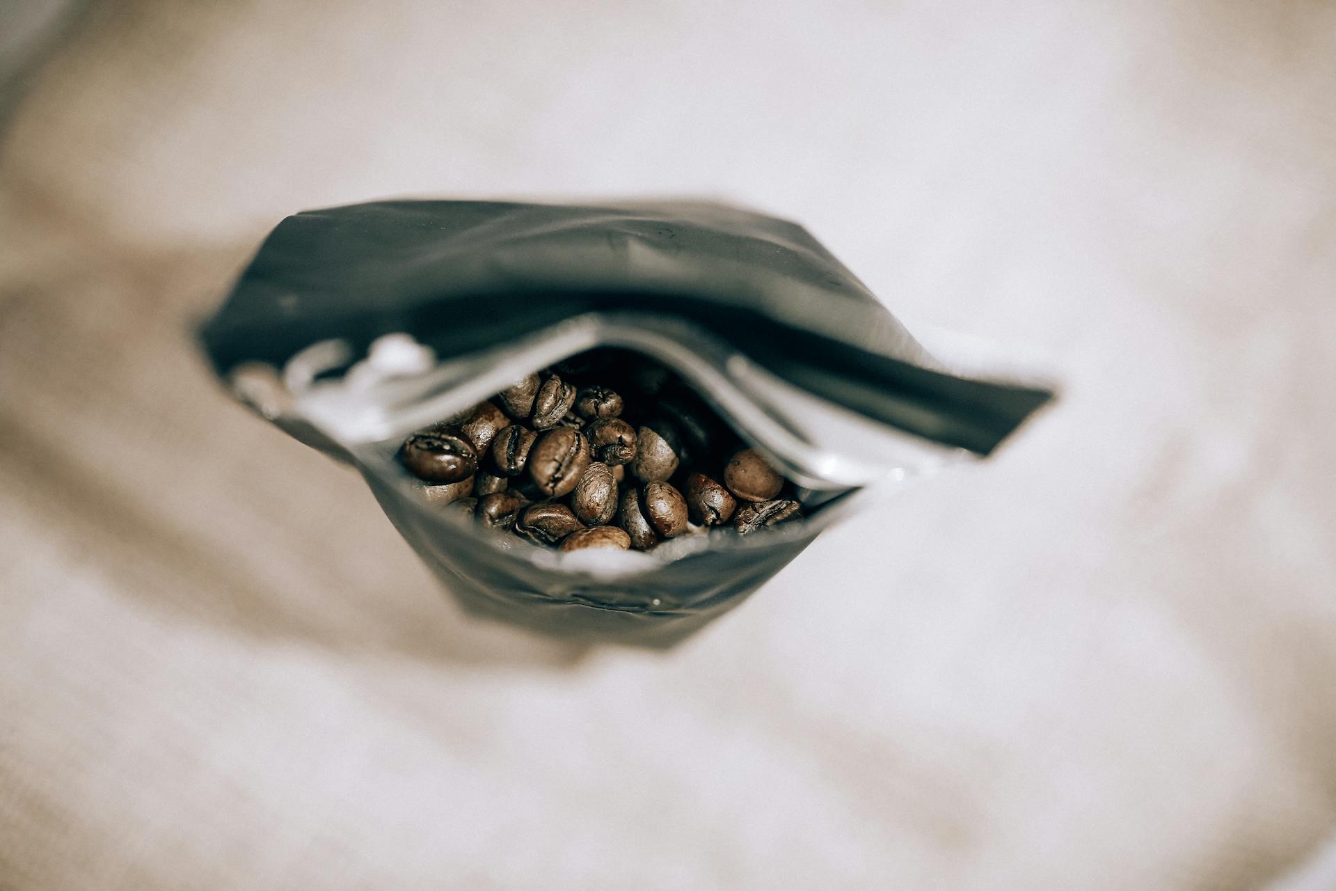 Top view of an open coffee bag revealing fresh roasted coffee beans with a soft focus.