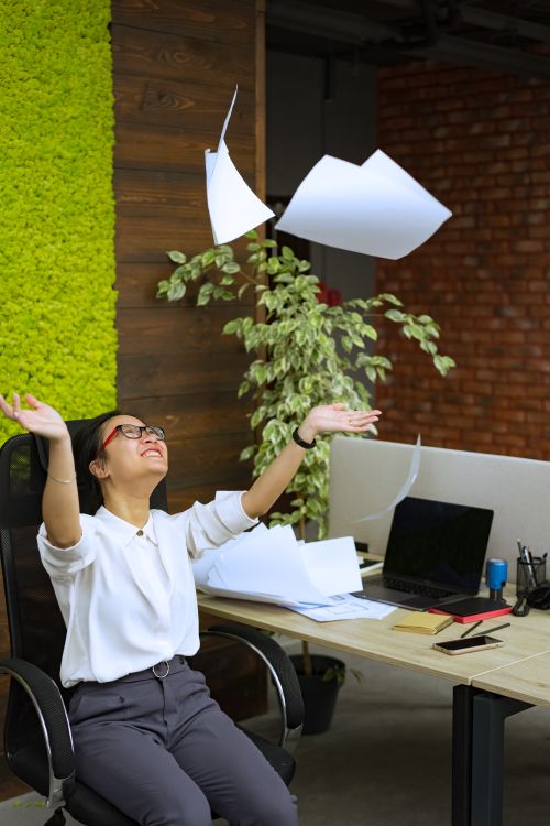 Free Happy Asian woman tossing papers in a modern office, celebrating success and freedom. Stock Photo