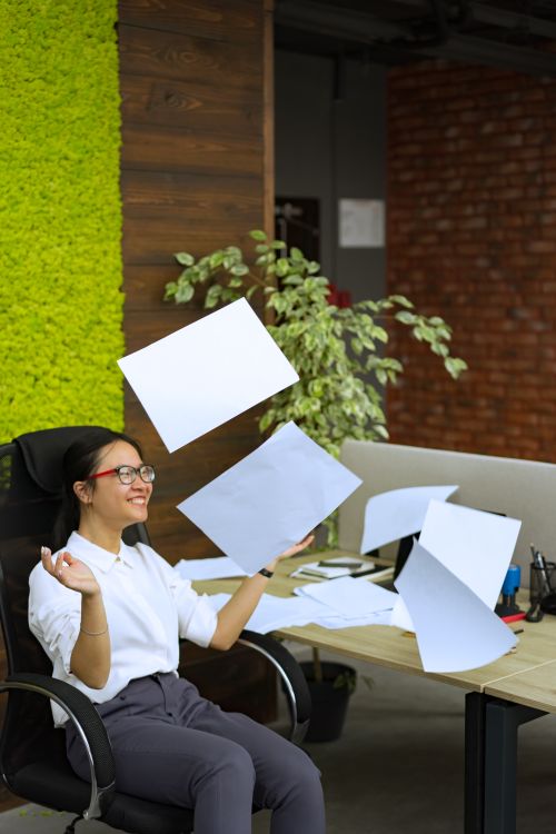 Free Joyful office worker celebrating by tossing papers in a modern workspace. Stock Photo