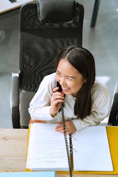 Asian woman smiling while speaking on the phone in an office environment.