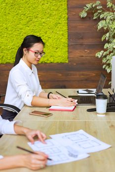 Asian woman in a modern office setting focused on her work with a laptop and notebook.