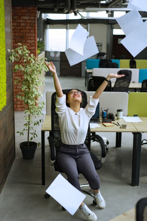 Free A delighted woman throws papers in the air, celebrating in a contemporary office setting. Stock Photo