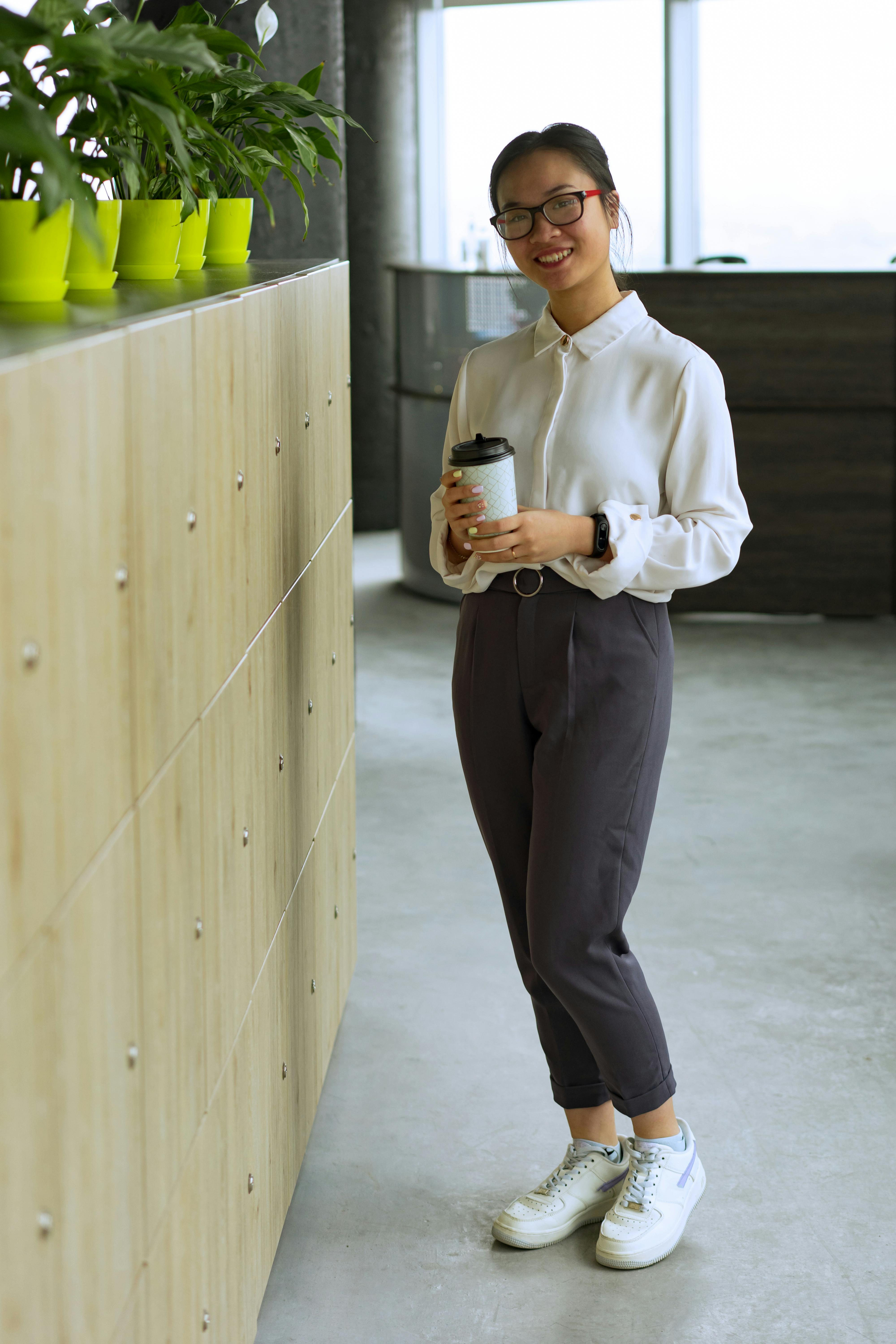 Happy woman holding a coffee cup, standing in a bright modern office space.