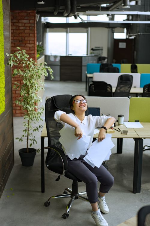 Free Asian woman laughing and relaxing in a brightly lit modern office. Stock Photo