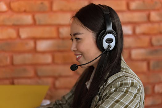Side view of an Asian woman wearing a headset working in an indoor office environment.