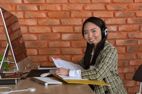 Free Smiling Woman with Headset Holding Files at Work Stock Photo