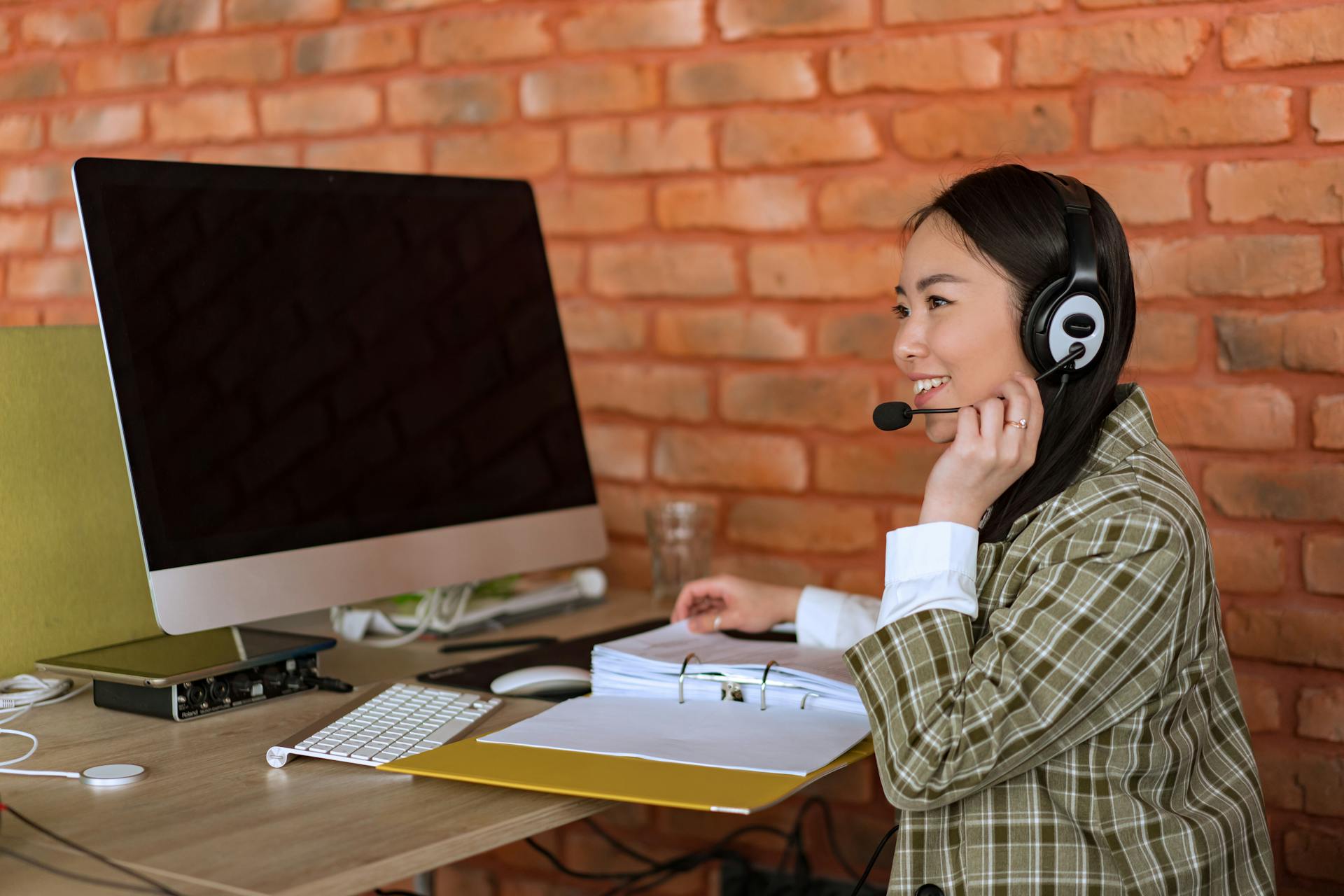 Smiling female call center agent working at desk with computer and headset.