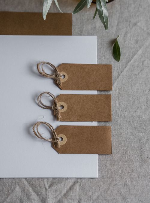 Free Three brown paper tags on a linen surface with olive leaves, perfect for branding or decoration. Stock Photo