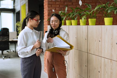 Free Two professional women discuss work while reviewing documents in a modern office setting. Stock Photo
