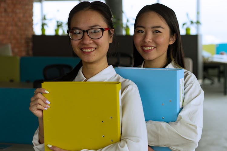 Women Smiling And Holding Binders