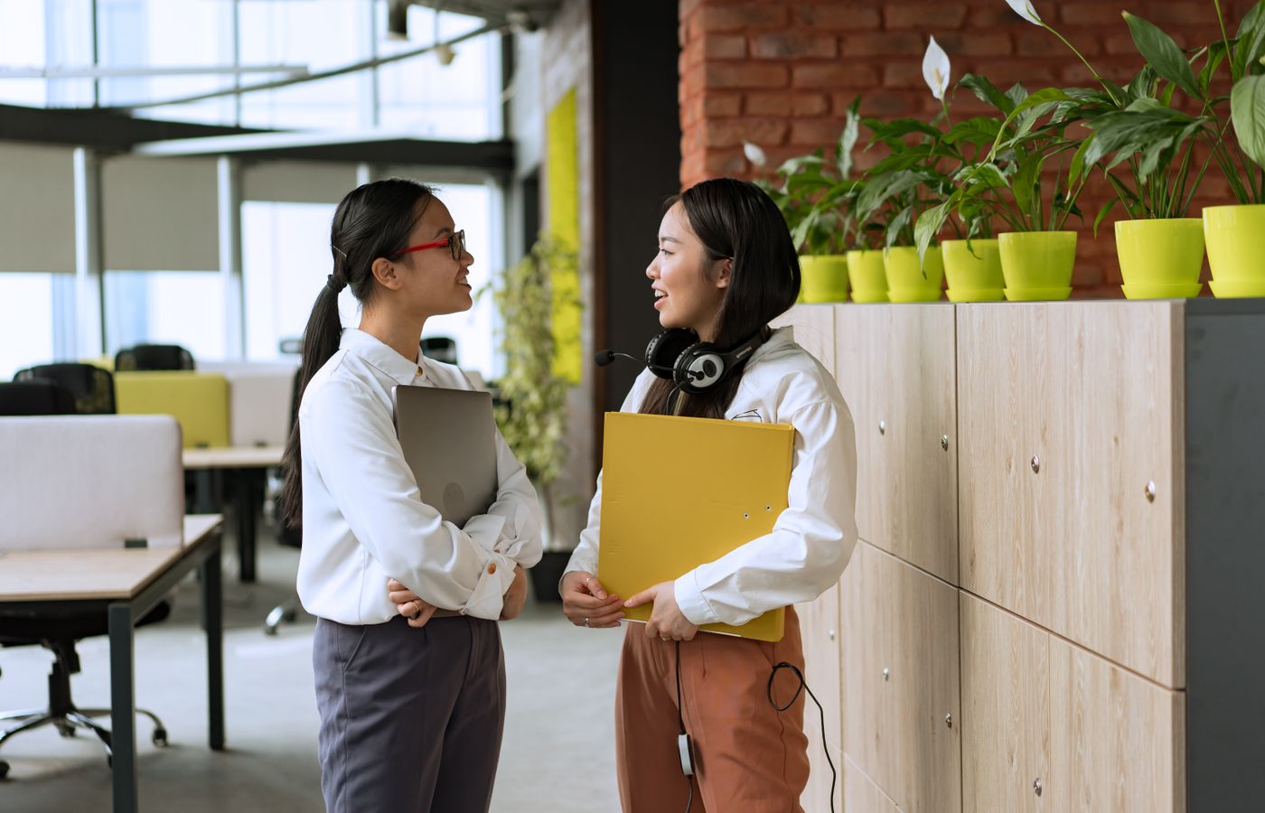 Two young professional women engaging in a conversation in a modern office setting.
