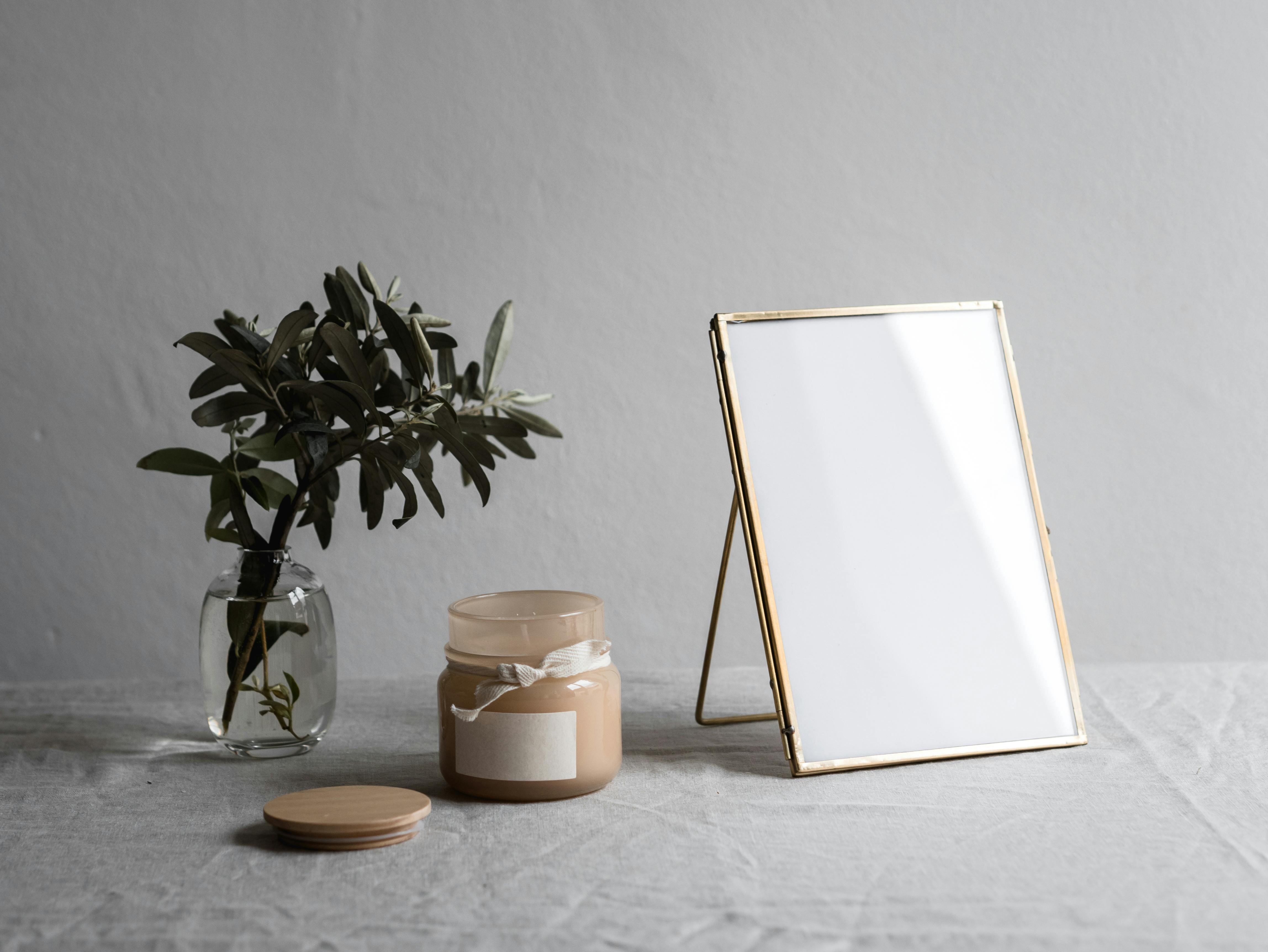 Elegant minimalist arrangement with plant, candle, and blank photo frame on a table.