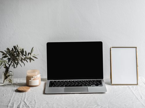 Free A sleek modern workspace featuring a laptop, candle, vase, and empty frame on a table. Stock Photo