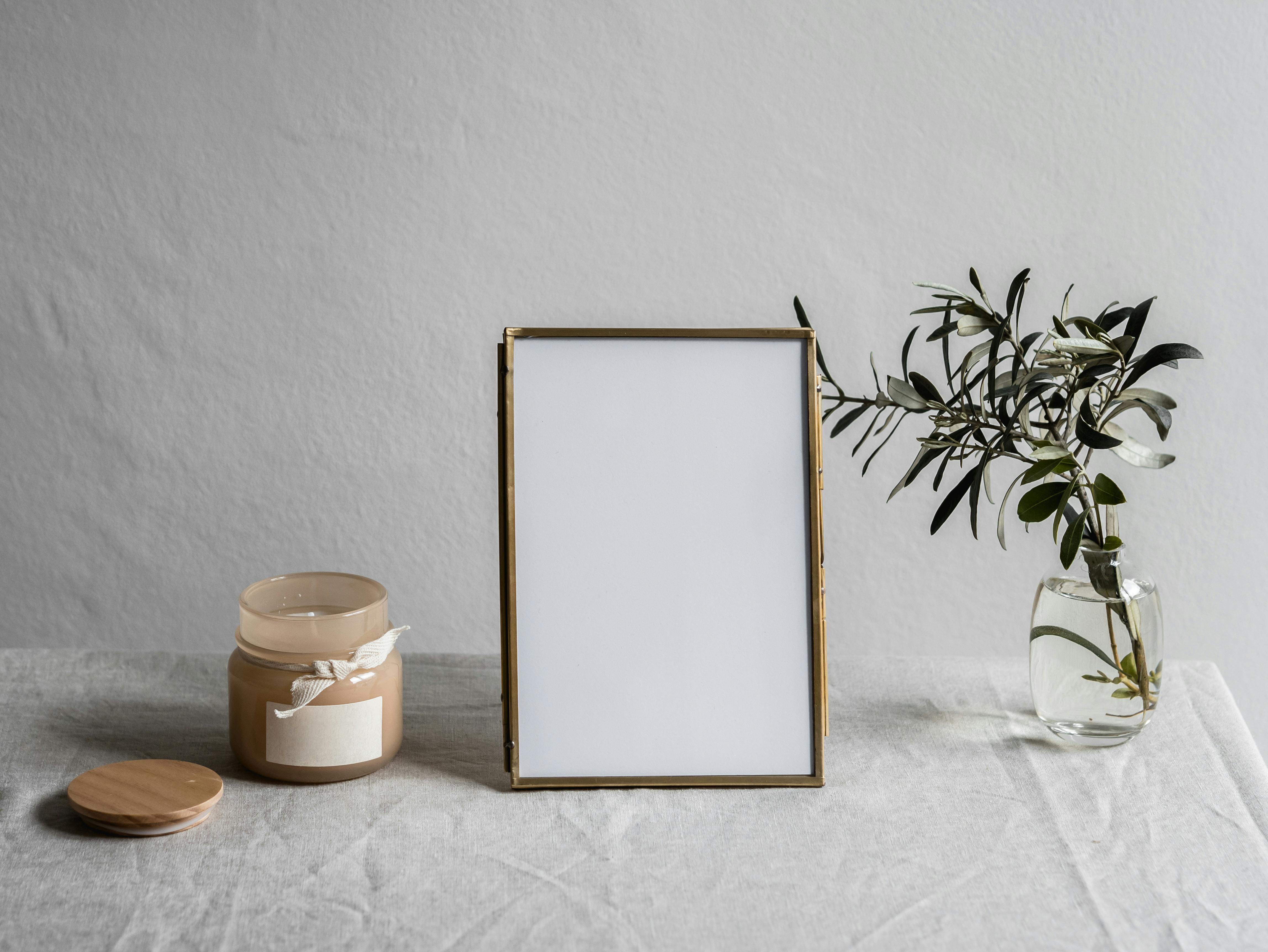 Free Empty Photo Frame Between a Glass vase with Plant and Jar with Candle Stock Photo