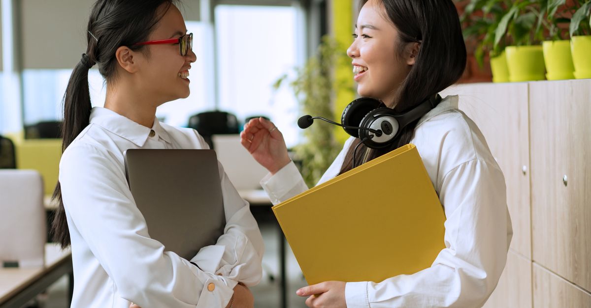 Two women colleagues conversing in a modern office, fostering teamwork.