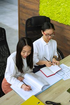 Two women collaborating at a desk in an indoor office environment, engaged in teamwork.