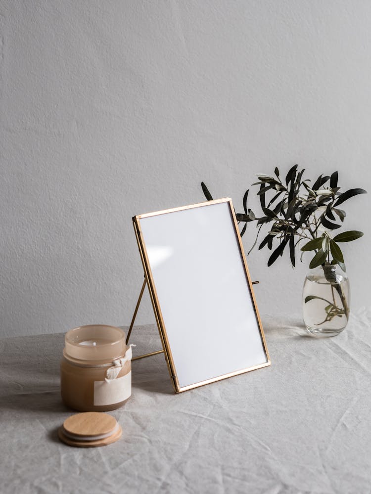 Empty Photo Frame Between A Glass Vase With Plant And Jar With Candle