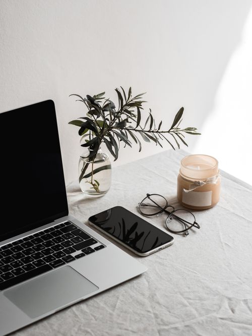 Free A minimalist indoor workspace setup with a laptop, smartphone, eyeglasses, candle, and plant. Stock Photo