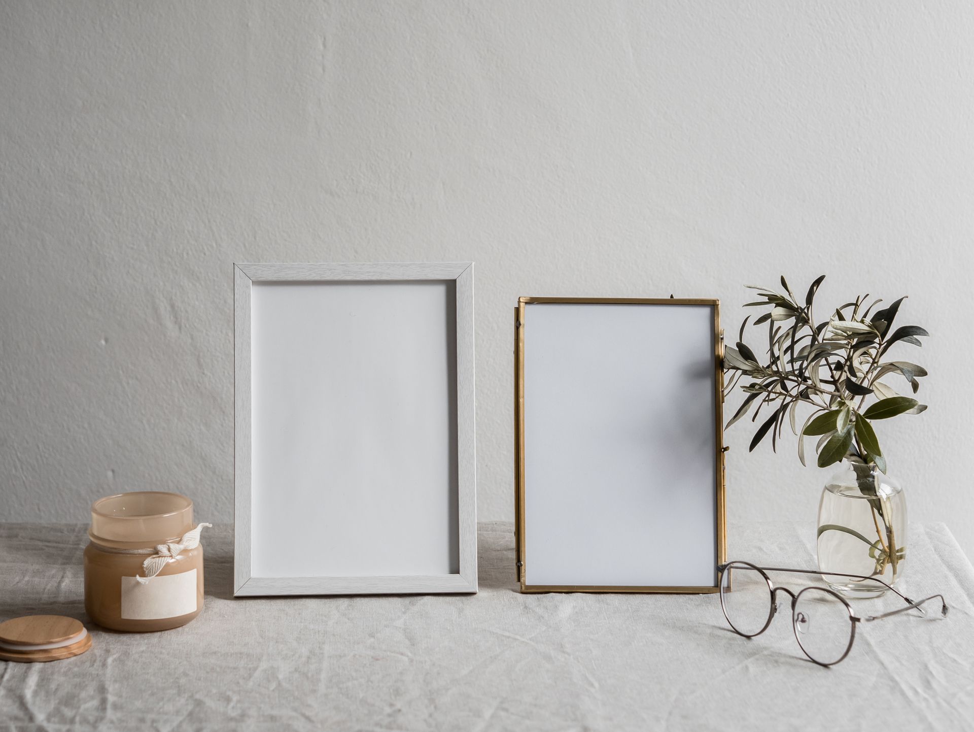 A serene minimalist still life featuring blank frames, glasses, and a candle on a neutral background.