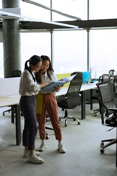 Two women reviewing documents in a spacious, well-lit modern office setting.