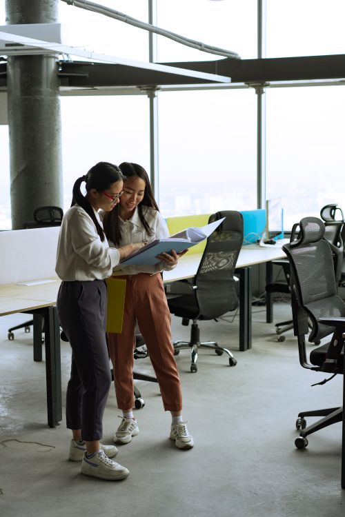 Free Two women reviewing documents in a spacious, well-lit modern office setting. Stock Photo