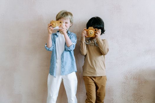 Two kids joyfully play with wooden toy cameras indoors, capturing fun moments.