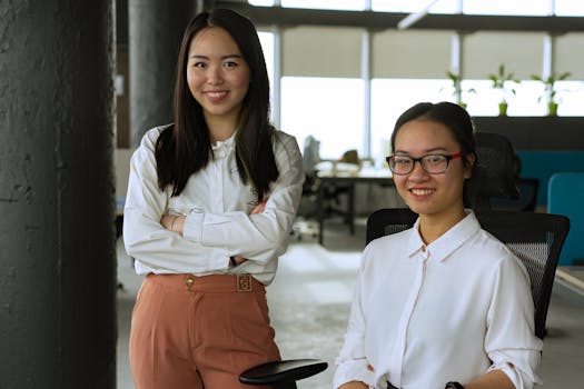 Two smiling women in an office, showcasing diverse workplace dynamics.