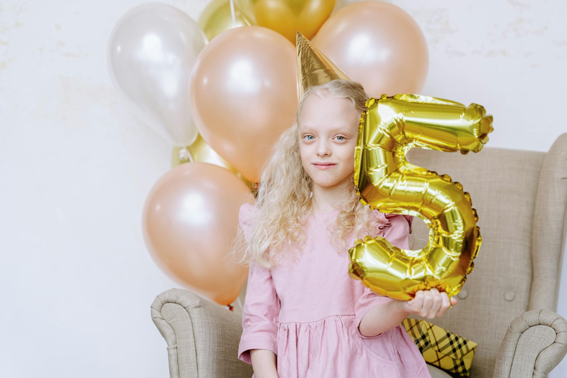 Young girl holding number five balloon at birthday party indoors.