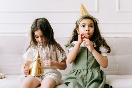 Free Two young girls in party hats enjoying a birthday celebration indoors. Stock Photo