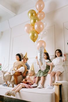 Group of kids enjoying a birthday party with balloons and party hats indoors.