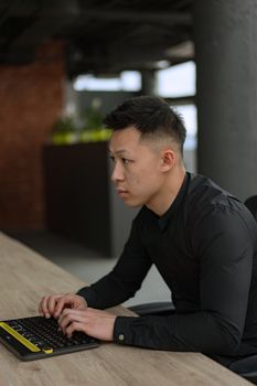 Asian man working on a keyboard in a modern office setting with a blurred background.