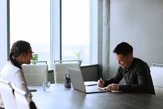 Two colleagues engaging in a corporate meeting with a laptop and documents.