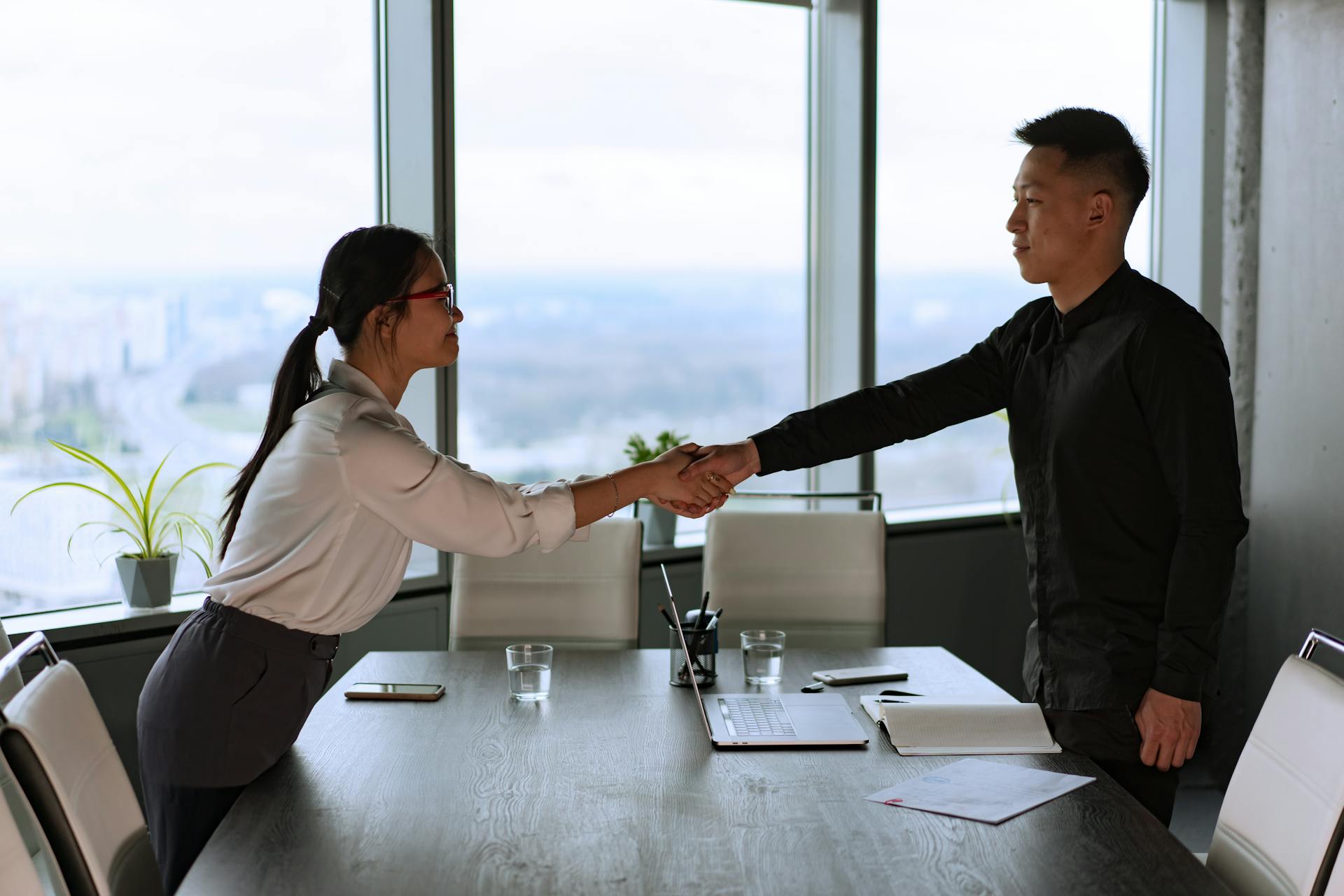 Professional coworkers exchange a handshake in a modern corporate office setting.