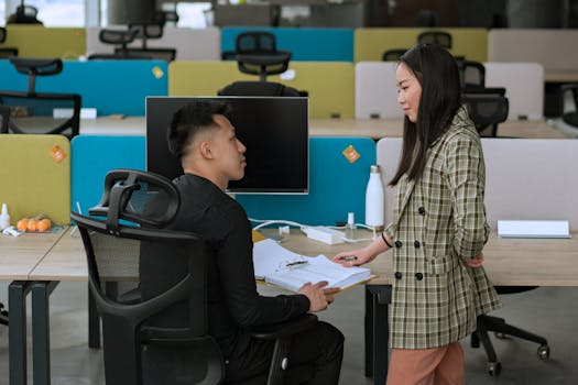 Two Asian professionals collaborating in a modern open office setting, discussing a project.