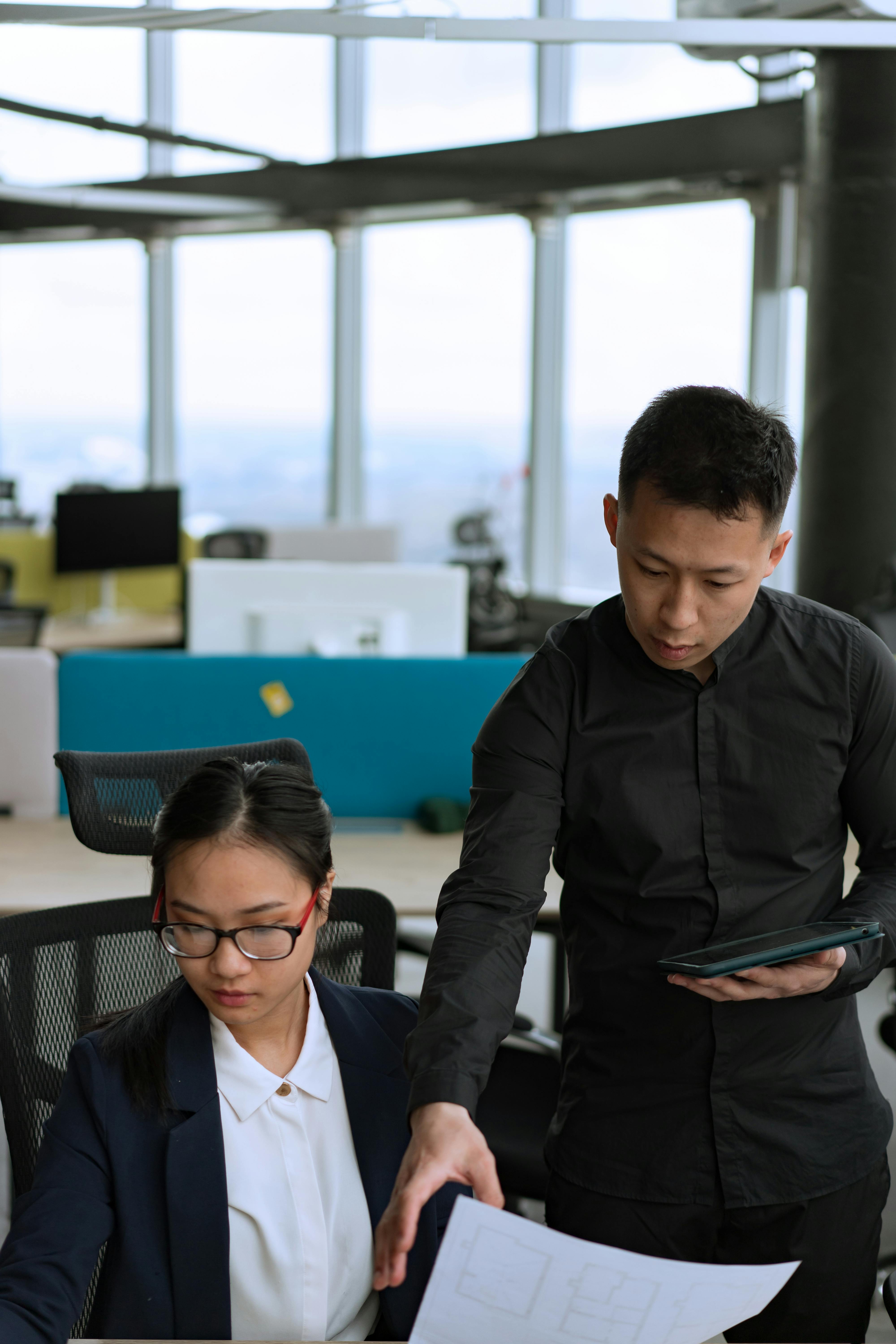 A man and woman collaborate in a modern office, emphasizing teamwork and skill sharing.