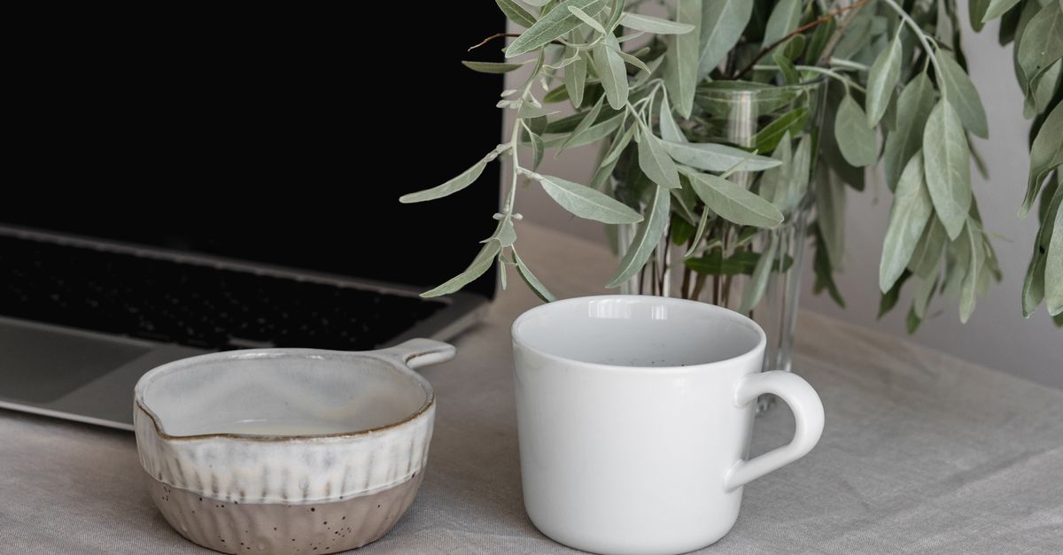 Tranquil workspace with a ceramic mug, bowl, and plant vase on a neutral tablecloth.