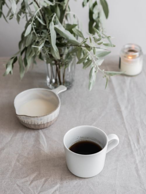 Free Elegant still life of black coffee, milk jug, and foliage on a linen tablecloth. Stock Photo
