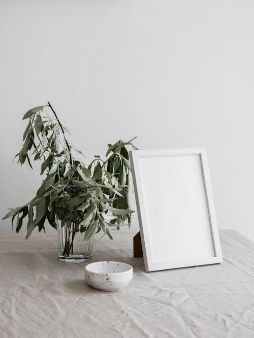 A White Photo Frame Beside a Glass Vase