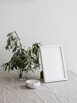A minimalist arrangement featuring a plant in a glass vase and an empty picture frame on a table.