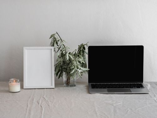 Free Minimalist workspace setup featuring a laptop, picture frame, candle, and plant on a table. Stock Photo