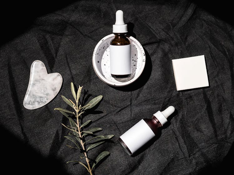 Brown Glass Bottles On Black Textile Beside Gua Sha And Leaves